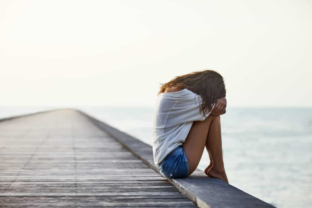 Sad depressed woman sitting on the pier hiding her face.