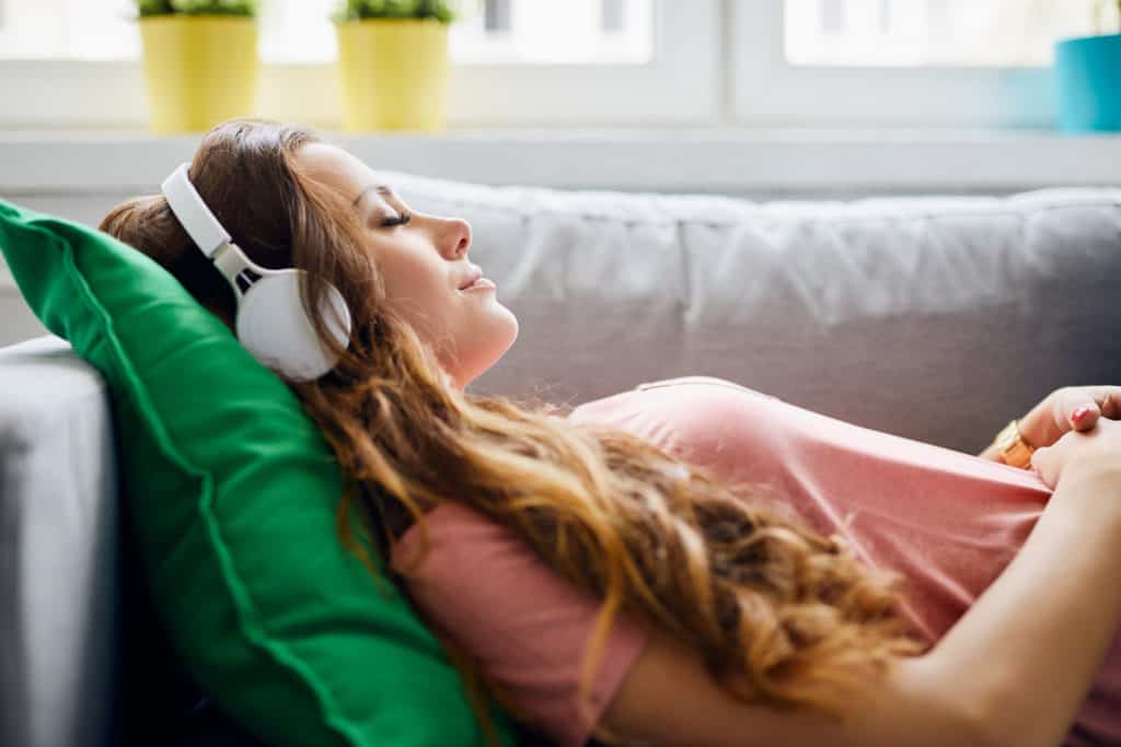 young woman lying on sofa with headphones on and closed eyes, relaxing