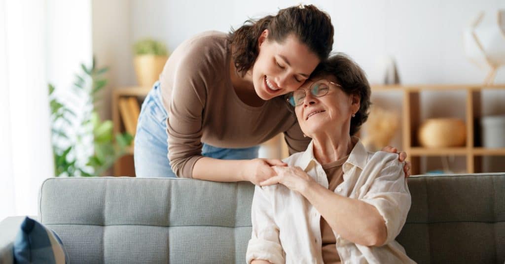 Daughter standing behind the couch hugging her mother.