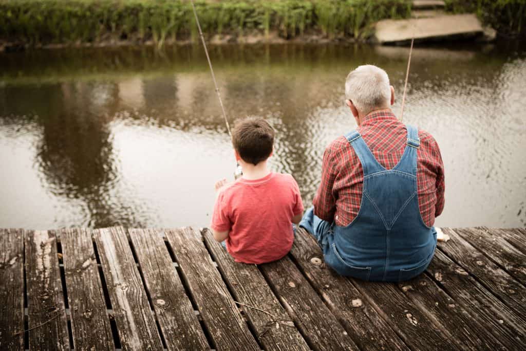 Grandfather and grandson fishing off a dock.