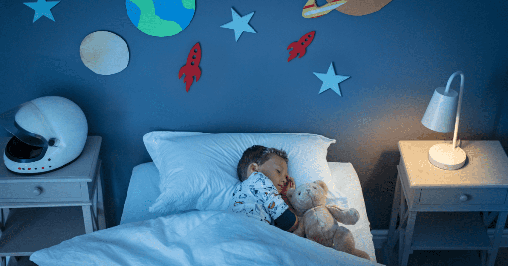 young boy sleeping with his teady bear in his space themed bedroom.