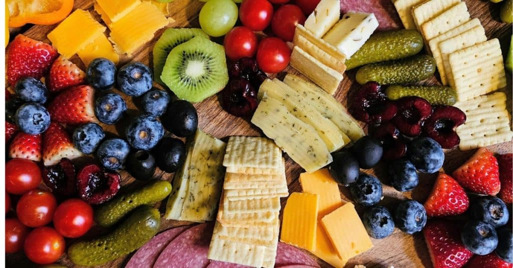 Charcuterie board of crackers, meats and bright colorful fruit.